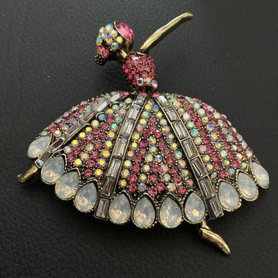 Sale Photo Thumbnail #201: Elaborate ballerina-form brooch decorated with pink, iridescent AB, and clear baguette rhinestones along with teardrop-shaped faux opalescent stones. Crafted in an antiqued gold-tone metal setting. Pin mechanism on back. Measures approximately 80mm in wid