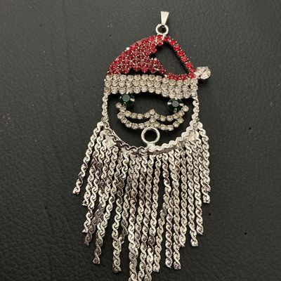 Sale Photo Thumbnail #149: Festive Santa Claus pendant featuring red, clear, and green rhinestones with silver-tone tassel fringe beard. Measures approximately 3.5 inches long (90 mm) by 1.75 inches wide (45 mm). Silver-tone metal backing with a pendant bail at the top. Good condit