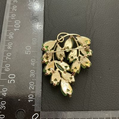 Sale Photo Thumbnail #178: A mid-century style vintage gold-tone brooch featuring frosted molded glass leaves in shades of green and yellow, accented with small green rhinestones. Measures approximately 50 mm x 40 mm (2 inches x 1.5 inches). Standard pin-back clasp mechanism on the