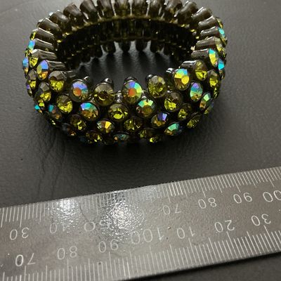 Sale Photo Thumbnail #216: A wide vintage-style stretch cuff bracelet set with multi-row olivine/olive green aurora borealis rhinestones in a dark gunmetal-tone setting. The iridescent stones display flashes of yellow, green, and blue. Measures approximately 30 mm wide with a flexi
