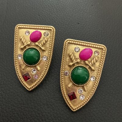 Sale Photo Thumbnail #205: Pair of vintage gold-tone clip-on earrings in a crest or shield design featuring crossed swords, colorful cabochons (green and fuchsia/pink), and clear plus red rhinestones. Each earring measures approximately 45 mm x 30 mm (1.75 in x 1.2 in). Show minor 