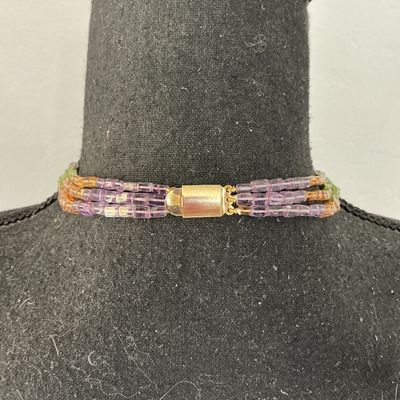 Sale Photo Thumbnail #265: A multi-strand beaded choker necklace featuring small, square cylinder beads in alternating sections of purple, light green, and amber orange. Finished with a gold-tone barrel clasp. In good pre-owned condition with no missing beads visible.