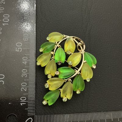 Sale Photo Thumbnail #176: A mid-century style vintage gold-tone brooch featuring frosted molded glass leaves in shades of green and yellow, accented with small green rhinestones. Measures approximately 50 mm x 40 mm (2 inches x 1.5 inches). Standard pin-back clasp mechanism on the