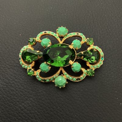 Sale Photo Thumbnail #164: Ornate vintage gold-tone openwork brooch featuring a large oval emerald-green faceted rhinestone center, accented by teardrop-cut green stones, light green cabochons, and small green rhinestone borders. Fitted with a standard pin back and rollover clasp. 