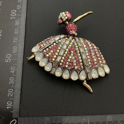 Sale Photo Thumbnail #202: Elaborate ballerina-form brooch decorated with pink, iridescent AB, and clear baguette rhinestones along with teardrop-shaped faux opalescent stones. Crafted in an antiqued gold-tone metal setting. Pin mechanism on back. Measures approximately 80mm in wid