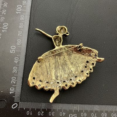 Sale Photo Thumbnail #204: Elaborate ballerina-form brooch decorated with pink, iridescent AB, and clear baguette rhinestones along with teardrop-shaped faux opalescent stones. Crafted in an antiqued gold-tone metal setting. Pin mechanism on back. Measures approximately 80mm in wid