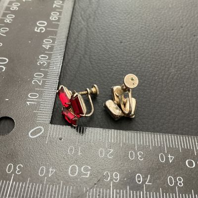 Sale Photo Thumbnail #254: Pair of vintage screw-back earrings featuring red baguette-cut rhinestone clusters in a silvertone or base metal setting. Each earring measures approximately 20mm x 15mm. Shows minor signs of age and wear to the metal finish consistent with age.