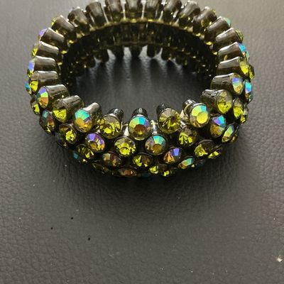 Sale Photo Thumbnail #214: A wide vintage-style stretch cuff bracelet set with multi-row olivine/olive green aurora borealis rhinestones in a dark gunmetal-tone setting. The iridescent stones display flashes of yellow, green, and blue. Measures approximately 30 mm wide with a flexi