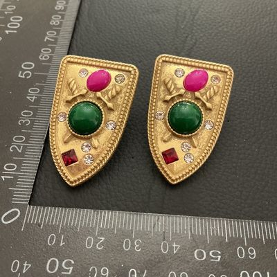 Sale Photo Thumbnail #206: Pair of vintage gold-tone clip-on earrings in a crest or shield design featuring crossed swords, colorful cabochons (green and fuchsia/pink), and clear plus red rhinestones. Each earring measures approximately 45 mm x 30 mm (1.75 in x 1.2 in). Show minor 