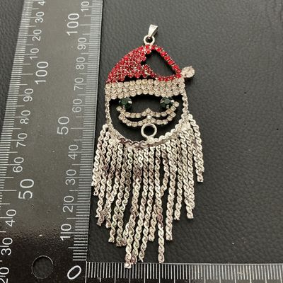 Sale Photo Thumbnail #151: Festive Santa Claus pendant featuring red, clear, and green rhinestones with silver-tone tassel fringe beard. Measures approximately 3.5 inches long (90 mm) by 1.75 inches wide (45 mm). Silver-tone metal backing with a pendant bail at the top. Good condit