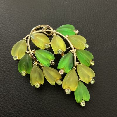 Sale Photo Thumbnail #174: A mid-century style vintage gold-tone brooch featuring frosted molded glass leaves in shades of green and yellow, accented with small green rhinestones. Measures approximately 50 mm x 40 mm (2 inches x 1.5 inches). Standard pin-back clasp mechanism on the