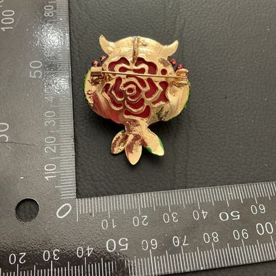 Sale Photo Thumbnail #225: Decorative owl-shaped costume brooch featuring a bold red center, amber-colored rhinestone eyes, green rhinestone accents along the sides, and multicolored leaf details. Gold-tone metal backing with standard pin closure and top loop. Measures approximatel