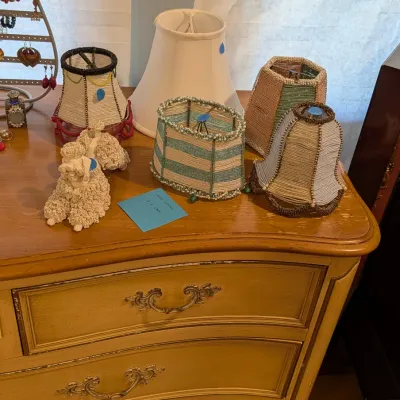 Assortment of vintage beaded mini lampshades and a white fabric shade resting on a French Provincial style chest of drawers alongside a...