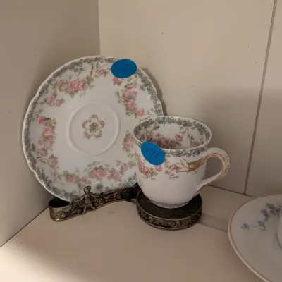 Vintage porcelain teacup and saucer set featuring delicate pink floral garlands and gilt accents, resting on ornate metal display stands.