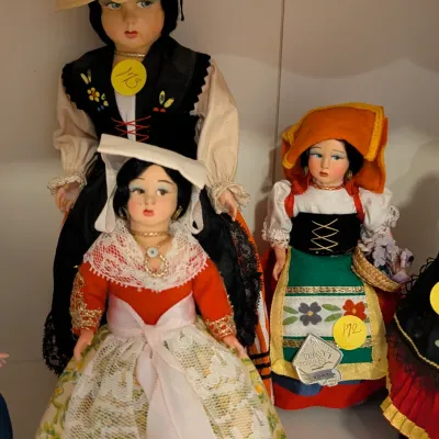 Collection of vintage European souvenir dolls dressed in traditional regional folk costumes, featuring detailed lace, embroidery, and...