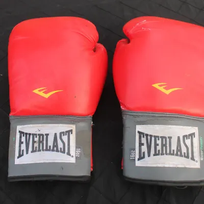 Sale Photo Thumbnail #77: Pair of red 16 oz Everlast EverFresh boxing gloves with grey hook-and-loop wrist cuffs, showing light surface wear.
