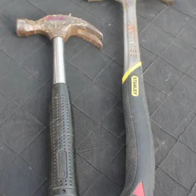 Sale Photo Thumbnail #75: Pair of claw hammers, including a Stanley AntiVibe model, showing moderate wear and surface rust on the steel heads.