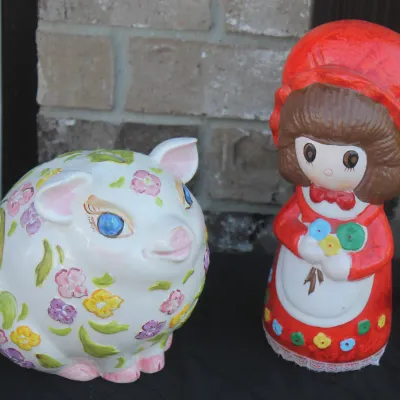 Sale Photo Thumbnail #34: Pair of vintage ceramic piggy banks, including a round floral-painted pig and a figure of a girl in a red bonnet.