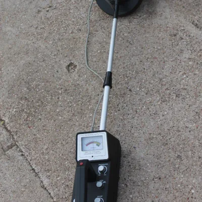 Sale Photo Thumbnail #53: Vintage Micronta 40173 VLF metal detector featuring an analog meter display and adjustable control dials, resting on a concrete surface.