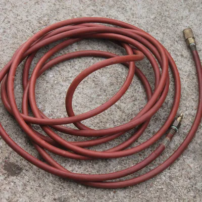 Sale Photo Thumbnail #50: Coiled red rubber air compressor hose with quick-connect brass fittings, showing typical surface wear from use.