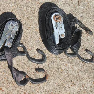 Sale Photo Thumbnail #70: Pair of heavy-duty black ratchet tie-down straps with metal hooks, showing light surface rust on the hardware.