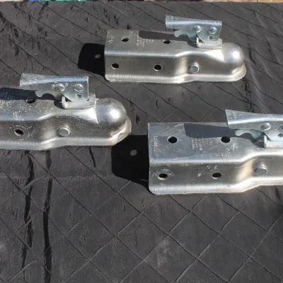 Sale Photo Thumbnail #4: Set of three galvanized steel trailer couplers with lever-locking mechanisms, showing light surface wear.