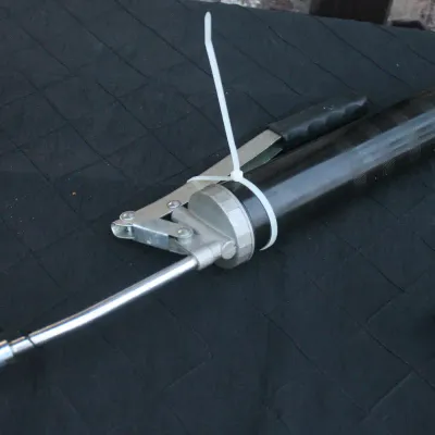 Sale Photo Thumbnail #58: Heavy-duty lever-action grease gun with rigid extension pipe, resting on a quilted moving pad.