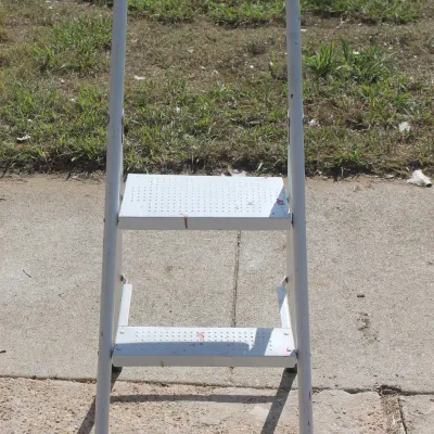 Sale Photo Thumbnail #44: White two-step folding metal ladder with top handle bar, showing minor wear and paint specks.