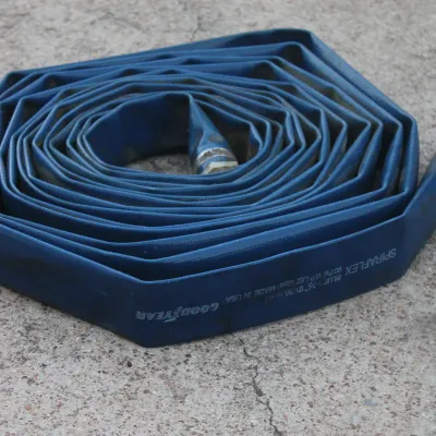 Sale Photo Thumbnail #26: Goodyear Spiraflex blue flat discharge hose coiled on concrete, showing attached hose couplings and light surface wear.