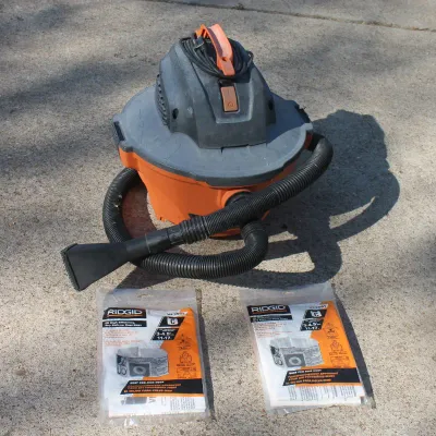 Sale Photo Thumbnail #36: Portable orange and gray Ridgid wet/dry shop vacuum with attached hose, nozzle, and two packages of replacement filter bags.