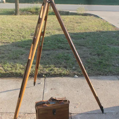 Sale Photo Thumbnail #17: Vintage surveyor's transit level mounted on a wooden tripod, complete with a fitted wooden carrying box featuring a leather strap.