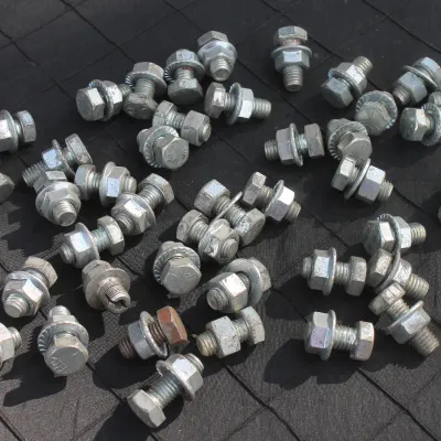 Sale Photo Thumbnail #63: Collection of galvanized hex head bolts fitted with washers and nuts arranged on a dark grid surface.