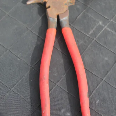 Sale Photo Thumbnail #74: Vintage fence pliers with red coated handles, showing surface rust on the metal head.