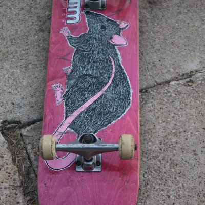 Sale Photo Thumbnail #57: Complete Alien Workshop skateboard featuring a pink deck with a rat graphic, silver trucks, and white wheels.