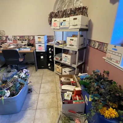 Sale Photo Thumbnail #43: Office room filled with storage items including bankers boxes on plastic shelving, file cabinets, and plastic totes filled with artificial floral arrangements.