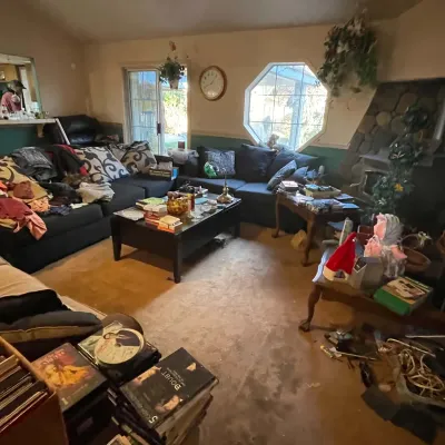 Sale Photo Thumbnail #67: Living room area featuring a large dark sectional sofa, a coffee table with various household items, and surrounding furniture.