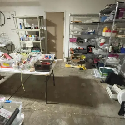 Sale Photo Thumbnail #76: Garage work and storage area featuring folding tables and metal shelving units packed with household items, plastic totes, and tools.