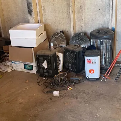Sale Photo Thumbnail #34: Collection of used space heaters, portable fans, power cords, and cardboard boxes stored in a garage or shed area.