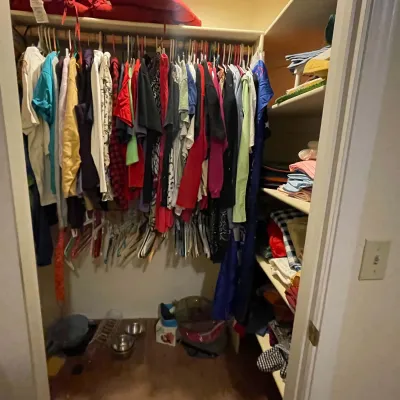 Sale Photo Thumbnail #89: Walk-in closet filled with various men's and women's clothing items, including shirts, jackets, folded linens, and pet supplies on the floor.
