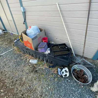 Sale Photo Thumbnail #28: Outdoor utility equipment including a large plastic storage box, long-handled yard tools, a metallic wash basin filled with rusty metal hardware, and various loose storage containers.