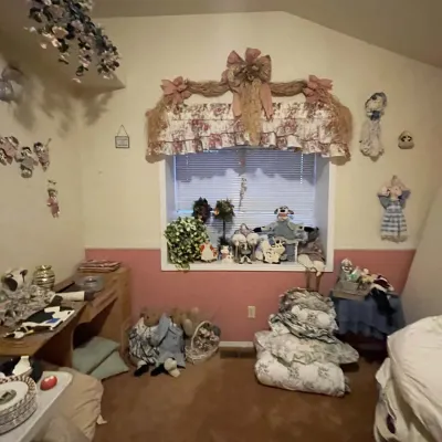 Sale Photo Thumbnail #88: A room filled with country-style decor including plush dolls, teddy bears, folded bedding stacks, wall-mounted crafts, and a floral window valance.