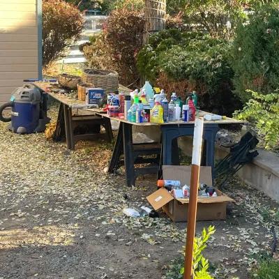 Sale Photo Thumbnail #48: Assorted yard and workshop supplies displayed on sawhorse tables outdoors, including cleaning chemicals, aerosol spray cans, baskets, and a Shop-Vac wet/dry vacuum.
