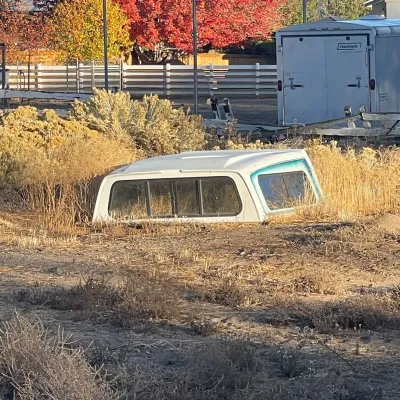 Sale Photo Thumbnail #31: White fiberglass pickup truck camper shell with side windows, resting in tall dry grass outdoors.
