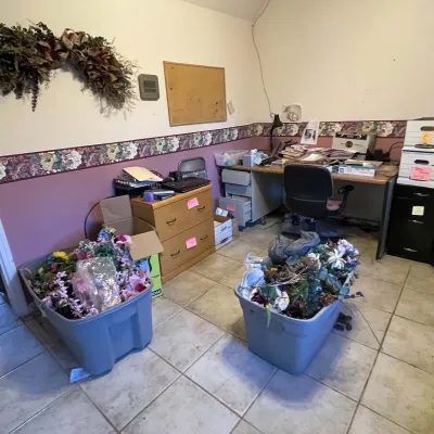Sale Photo Thumbnail #44: Home office filled with assorted supplies, including plastic storage totes of faux flowers, a wooden two-drawer file cabinet, and a large office desk.