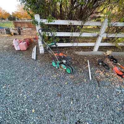 Sale Photo Thumbnail #38: Gas-powered lawn edger with a green frame and wheels, shown alongside gas cans and power lawn tools near a white fence.