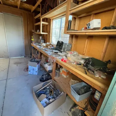 Sale Photo Thumbnail #53: Workshop and shed area with long wooden workbenches, wall shelving, and various tools, hardware, and supplies.