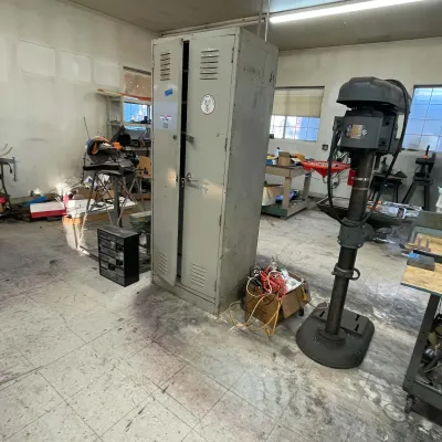 Sale Photo Thumbnail #59: Vintage heavy-duty industrial floor-standing drill press alongside a tall grey metal storage locker cabinet in a workshop.