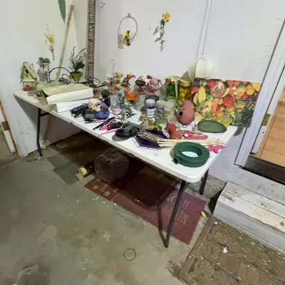 Sale Photo Thumbnail #70: White folding utility table displaying an assortment of household goods, including craft supplies, artificial plants, kitchenware, and decorative knick-knacks.