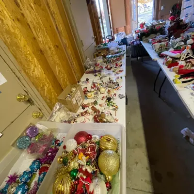 Sale Photo Thumbnail #10: Large collection of vintage and modern Christmas decorations, including colorful glass baubles, figurines, and holiday crafts displayed on folding tables.