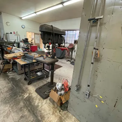 Sale Photo Thumbnail #23: Vintage heavy-duty floor-standing drill press in a workshop, surrounded by rolling tool carts, workbenches, and various shop equipment.